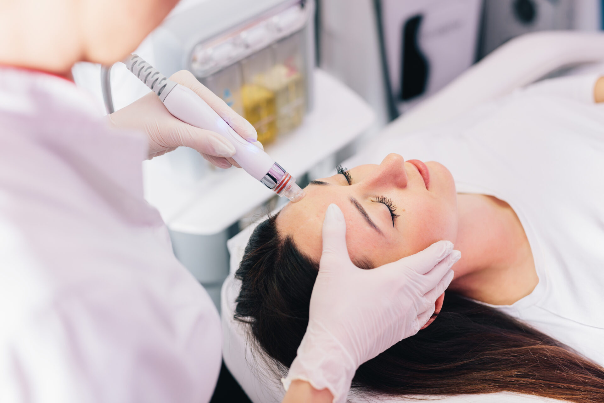 Cosmetologist doing hydrafacial treatment on woman face in beauty clinic