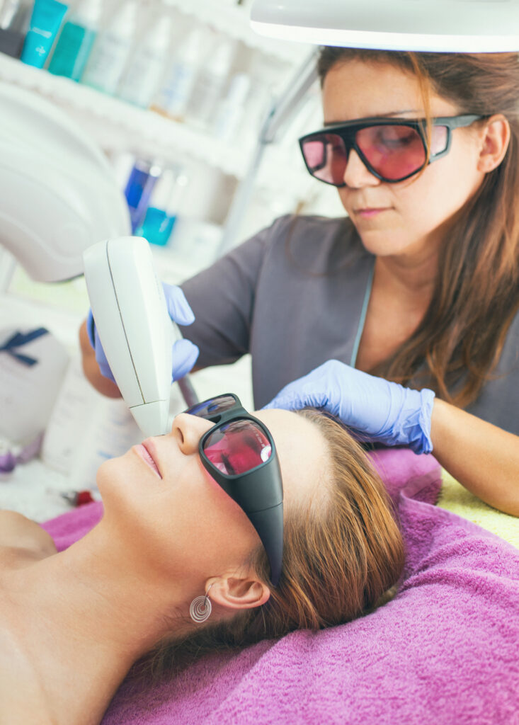 Close-up of a woman receiving facial laser hair removal treatment by a beautician at Reimagine Beauty Lancaster Med Spa, both wearing protective eyewear.